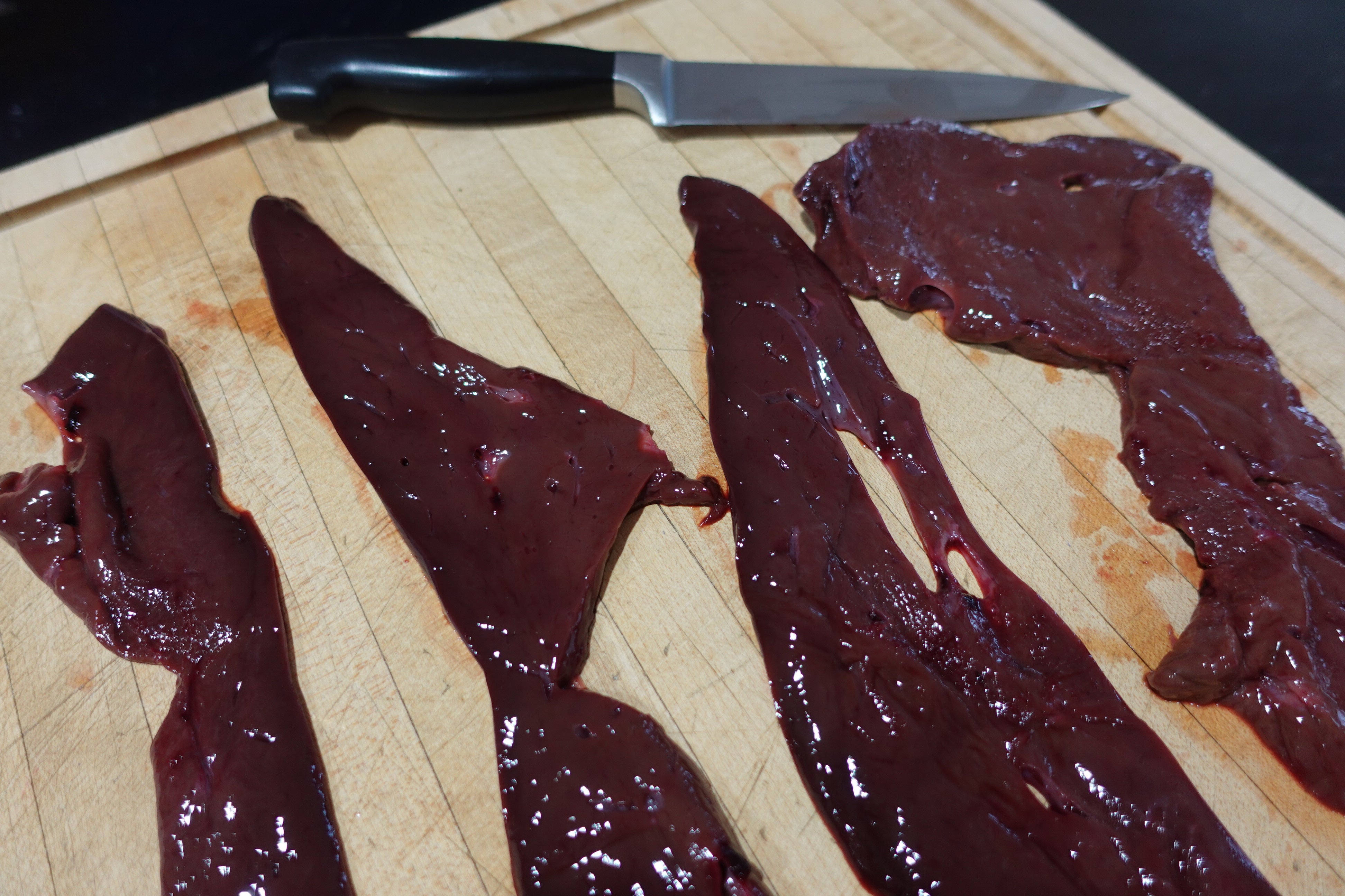 Fresh raw beef liver hand-sliced on a cutting board